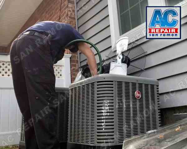 This image displays our dedicated service technician performing comprehensive scheduled HVAC maintenance at a customer's residence in San Ramon, CA. The technician is captured in the process of cleaning the outdoor portion of the condenser unit, which is a crucial component of the home's heating and cooling systems. He meticulously tends to the fan, condenser coil, and compressor pump, ensuring they are debris-free and functioning optimally. This thorough maintenance approach exemplifies our commitment to maintaining the longevity and efficiency of HVAC systems. The image provides a visual insight into our detailed maintenance procedures and links to our HVAC maintenance service page for further information.