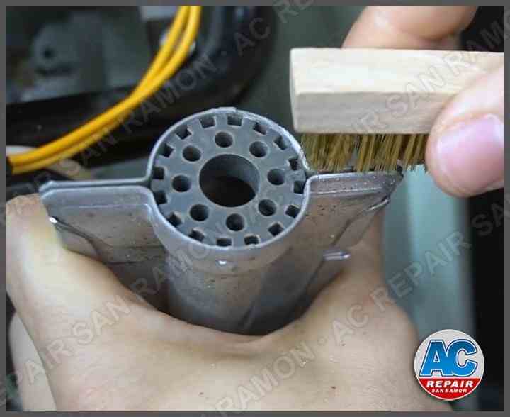 HVAC technician performing routine furnace maintenance with wire brush cleaning in San Ramon home