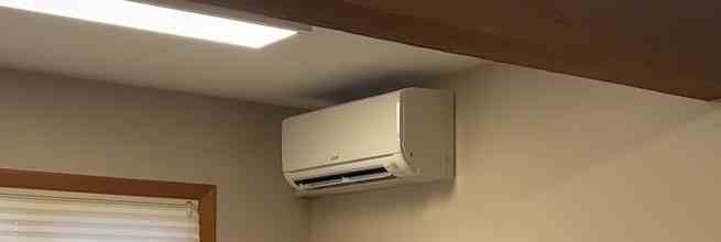 A wall-mounted mini-split air conditioner installed high on the wall of a room with beige walls, near a window with white blinds, bearing the logo of AC Repair San Ramon.